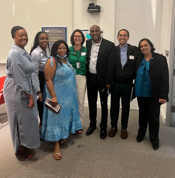 A photo of Georgetown LEND professors Rachel Brady and Pamala Trivedi with a group of LEND trainees at the Annual Conference. The diverse group is dressed nicely and smiling, and are standing in an auditorium.