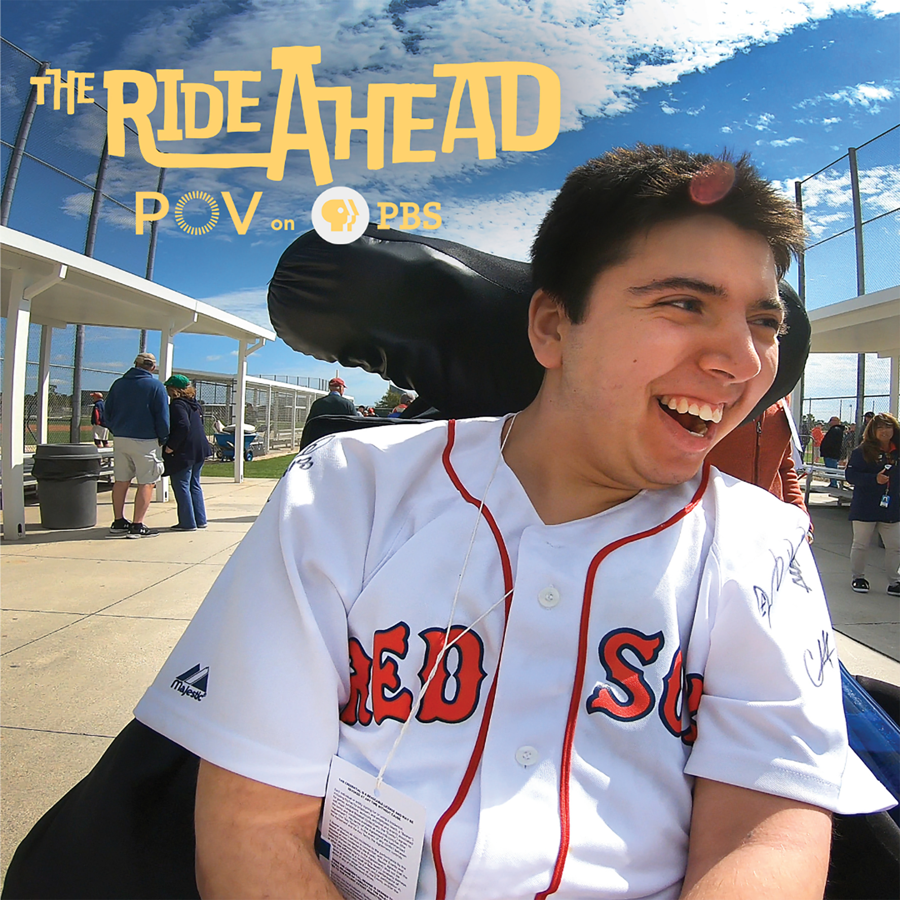 Samuel smiling in his wheelchair wearing a Red Sox jersey at a baseball game.